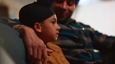 Close-Up-Of-Loving-Sikh-Father-And-Son-Wearing-Turbans-Sitting-On-Sofa-At-Home-Talking-Together-Shot-In-Real-Time